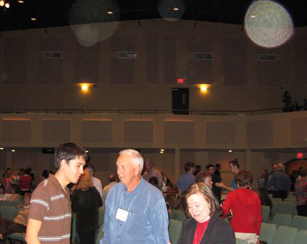 Three people in an auditorium, with a large greenish circular light spot (angel orbs) above them