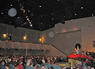 Auditorium crowd beneath a high ceiling, with large circular light spots (angel orbs) in the photograph