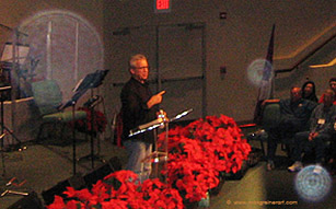 Speaker at a lectern with red flowers, with circular light spots (angel orbs) in the photograph