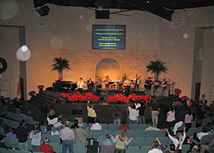 Rear view of a congregation facing a stage cross, with circular light spots (angel orbs) in the photograph