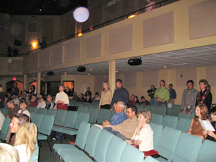 People beneath an auditorium balcony, with circular light spots (angel orbs) in the photograph
