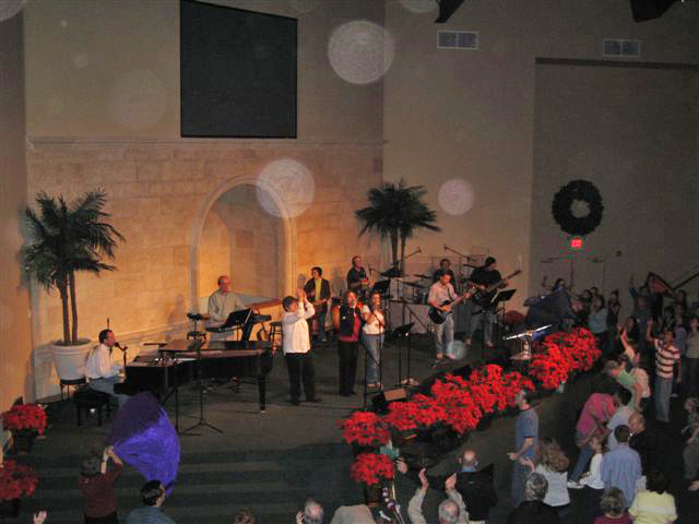 Church stage with a wall cross and red flowers, with circular light spots (angel orbs) in the photograph
